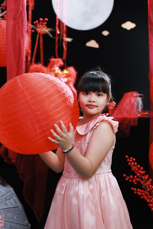 Free Young girl in festive dress holding red lantern under full moon during Lunar New Year celebration. Stock Photo