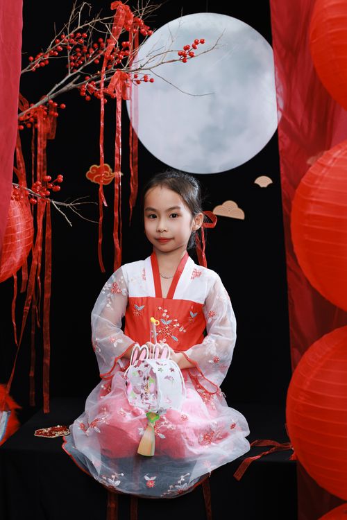 Free A young girl in a vibrant red traditional dress with festive decorations and a full moon backdrop. Stock Photo