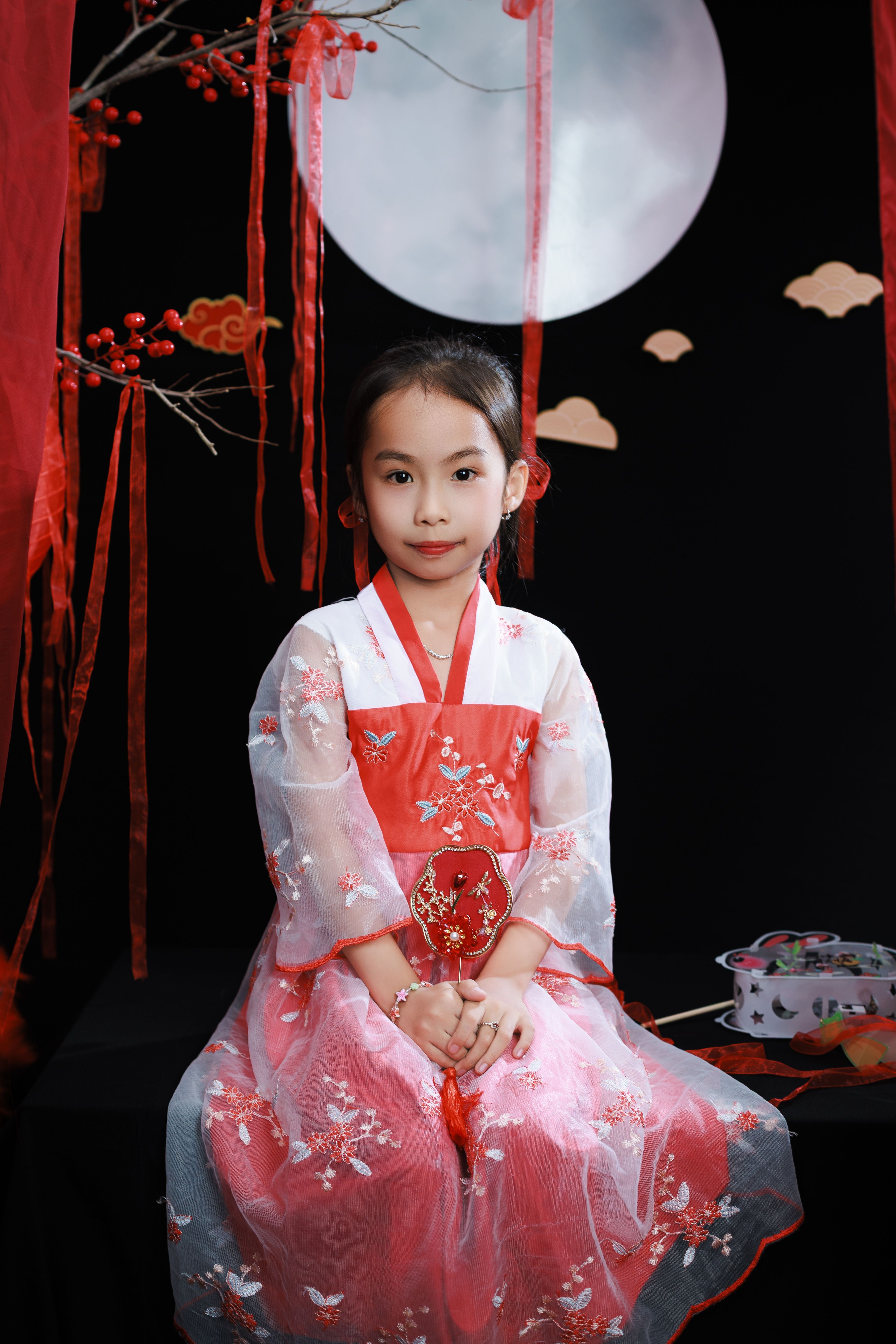 Young girl in traditional Asian dress posing during a cultural festival with moon and decorations.
