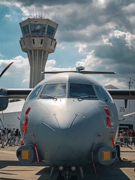 Front view of a military aircraft on runway with control tower in the background.