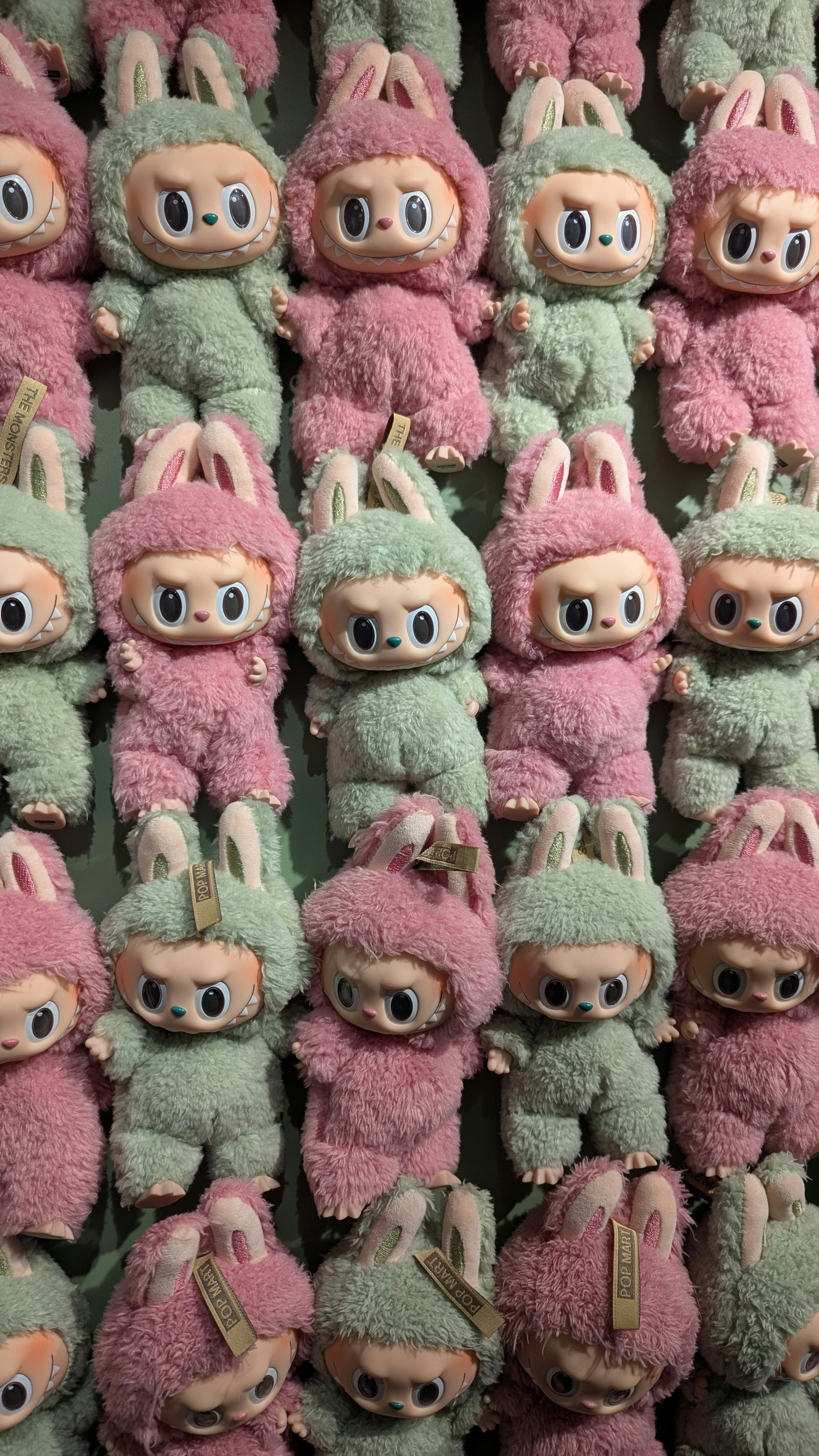 A vibrant wall of pastel plush toys with big eyes in green and pink colors.