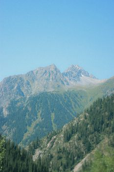 A stunning mountain range covered with lush green forest under a clear blue sky.