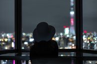一名女子在夜晚透过窗户，凝望着东京的城市灯光剪影