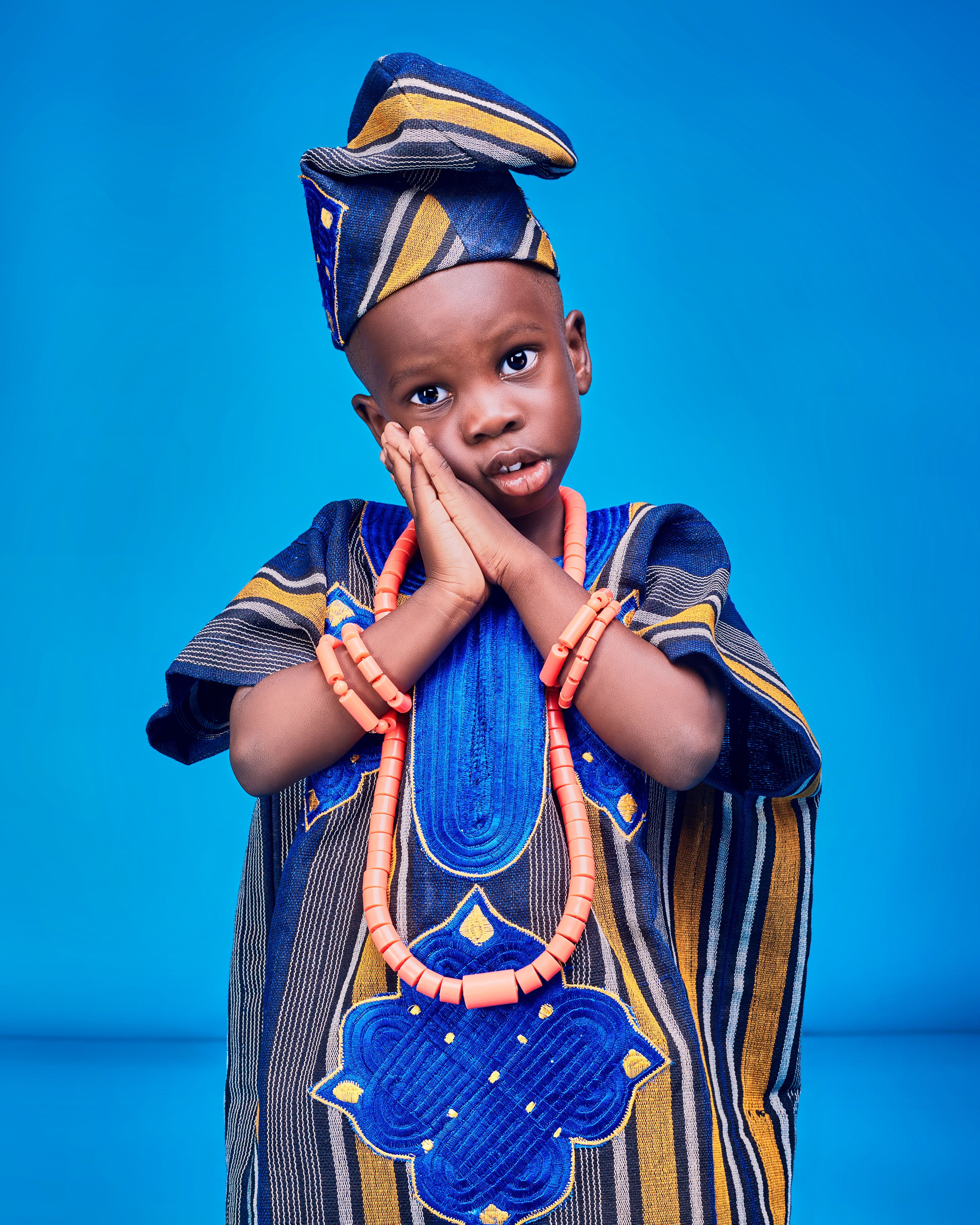 Adorable child in vibrant traditional African attire against a bright blue backdrop.