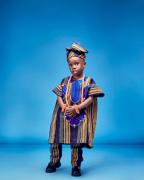 Free Smiling child wearing vibrant traditional African clothing against a blue background. Stock Photo