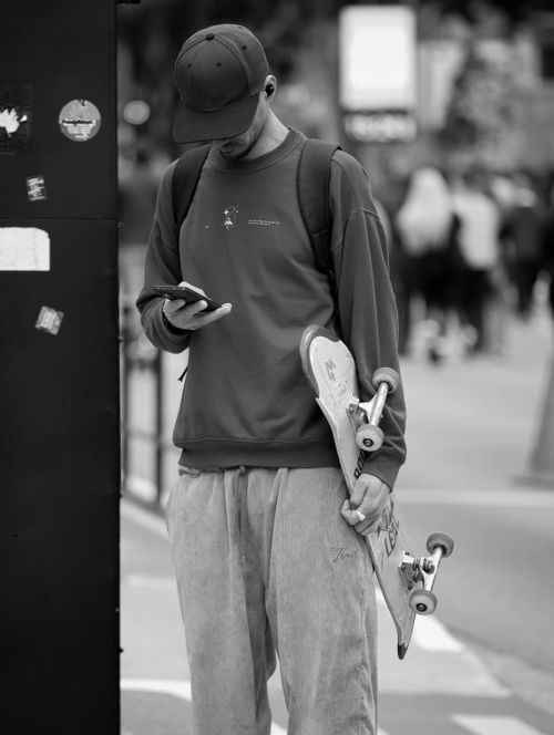 Free A young skater stands in a city holding a skateboard and checking his phone. Stock Photo