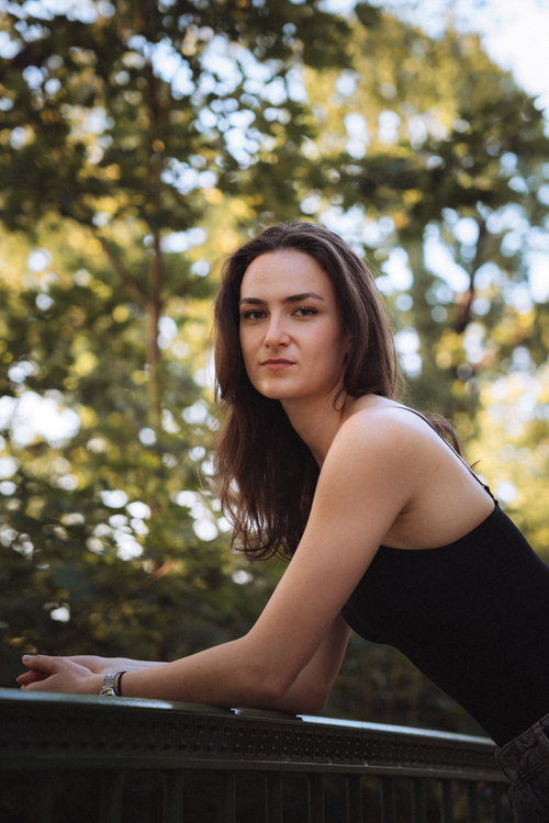 Free Portrait of a young woman leaning on a railing outdoors with trees in the background. Stock Photo