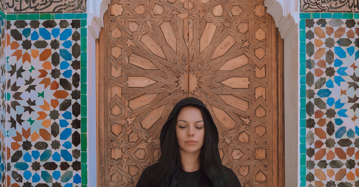 Woman meditating in a Moroccan architectural doorway with intricate mosaic tiles.