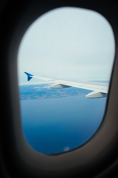 Free Aerial view from airplane window showing ocean and coastline under a clear sky. Stock Photo