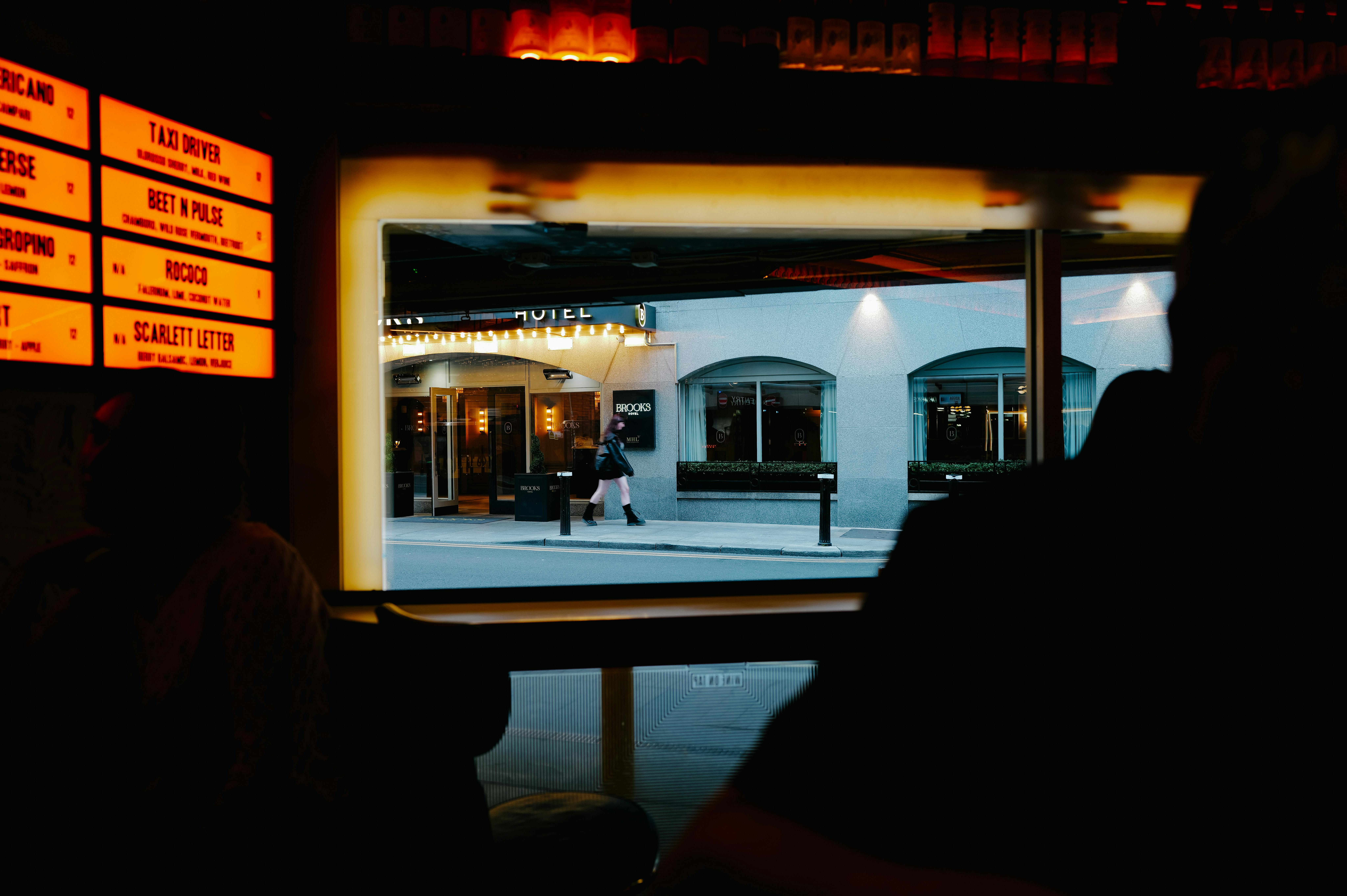 View from inside a dimly lit bar to a street outside with cafe and pedestrians.