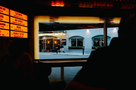 View from inside a dimly lit bar to a street outside with cafe and pedestrians.