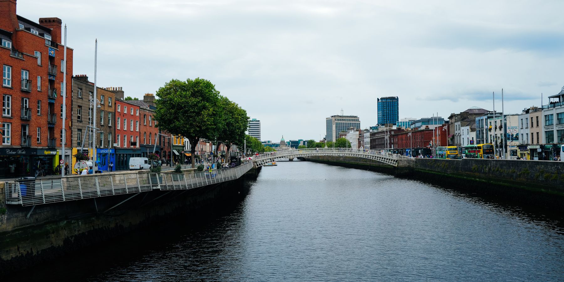 Scenic view of Dublin's Ha'penny Bridge over the River Liffey amidst urban architecture and vibrant city life.