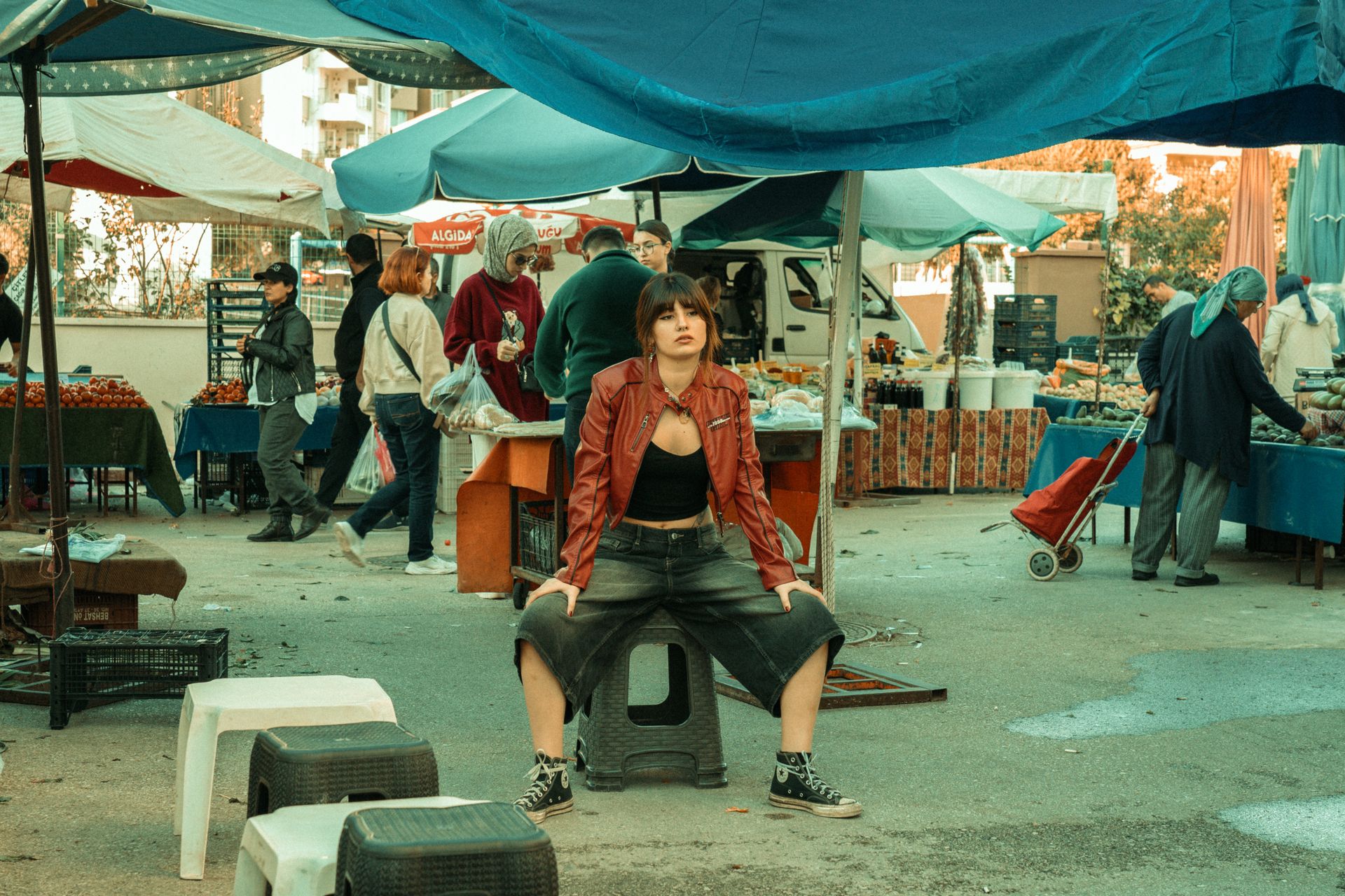 Confident woman in red jacket at a vibrant outdoor market scene.