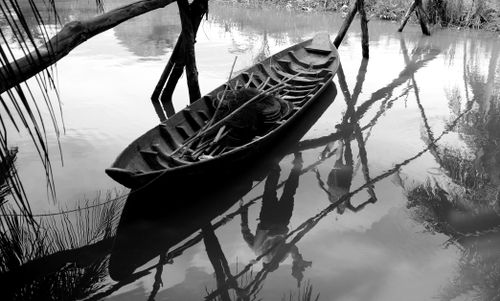 Free Black and white image of a canoe reflecting on calm water with surrounding trees. Stock Photo
