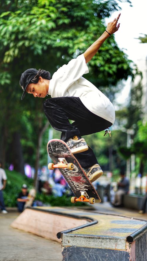 Free Energetic skateboarder performing a mid-air trick in a vibrant park setting, showcasing athletic skill and style. Stock Photo