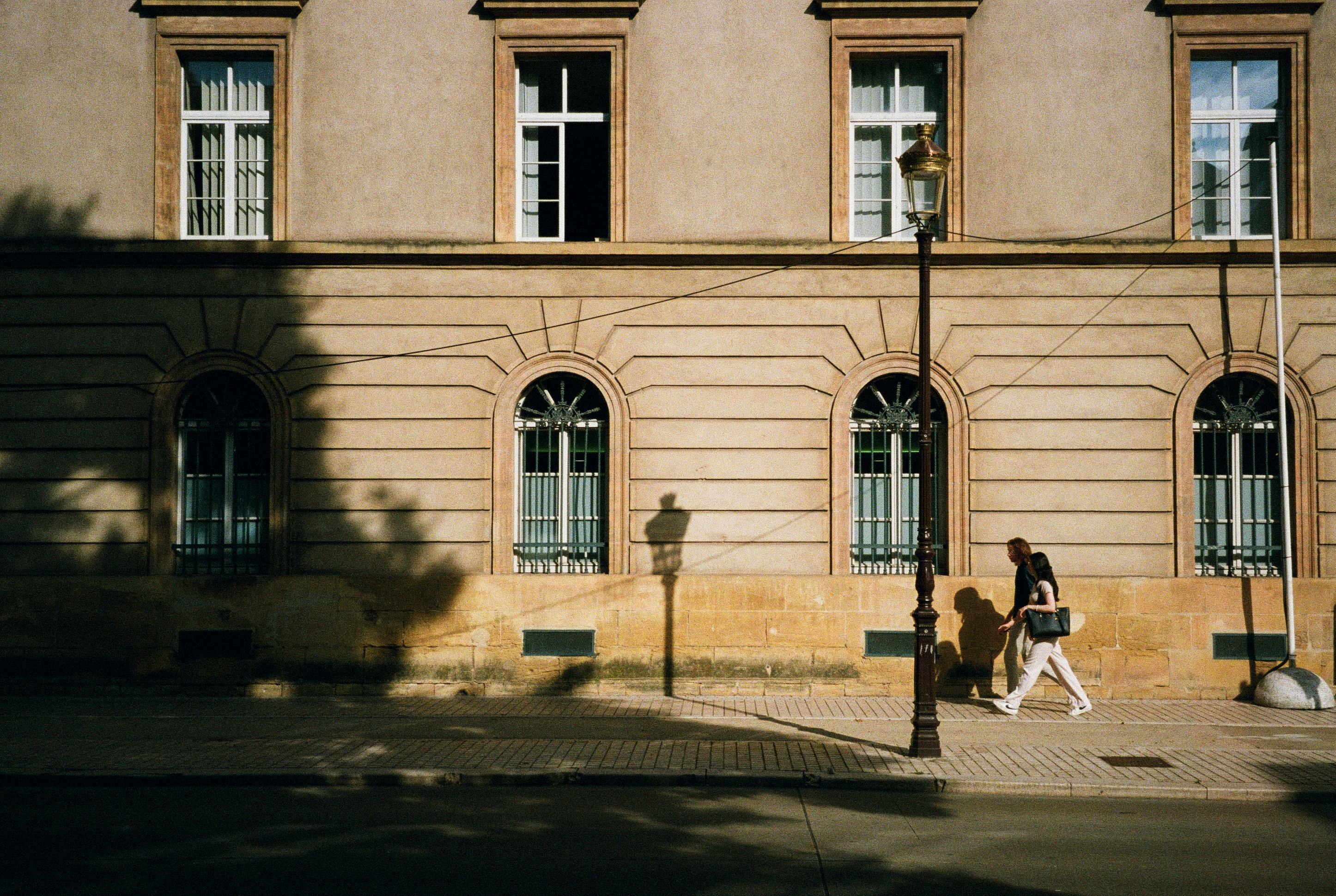 A person walks along a historic building in Metz, France, casting a shadow