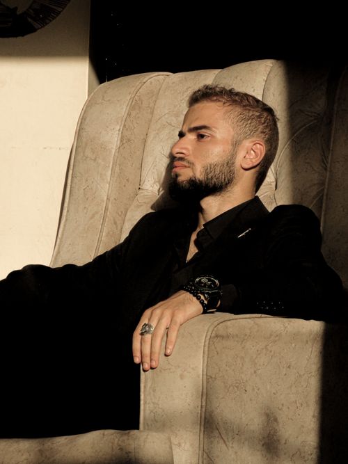 Free Bearded man in a suit sits thoughtfully in a sunlit beige armchair indoors. Stock Photo