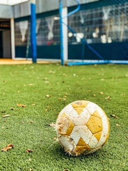 A worn-out soccer ball lies on an unkempt field, symbolizing forgotten play.