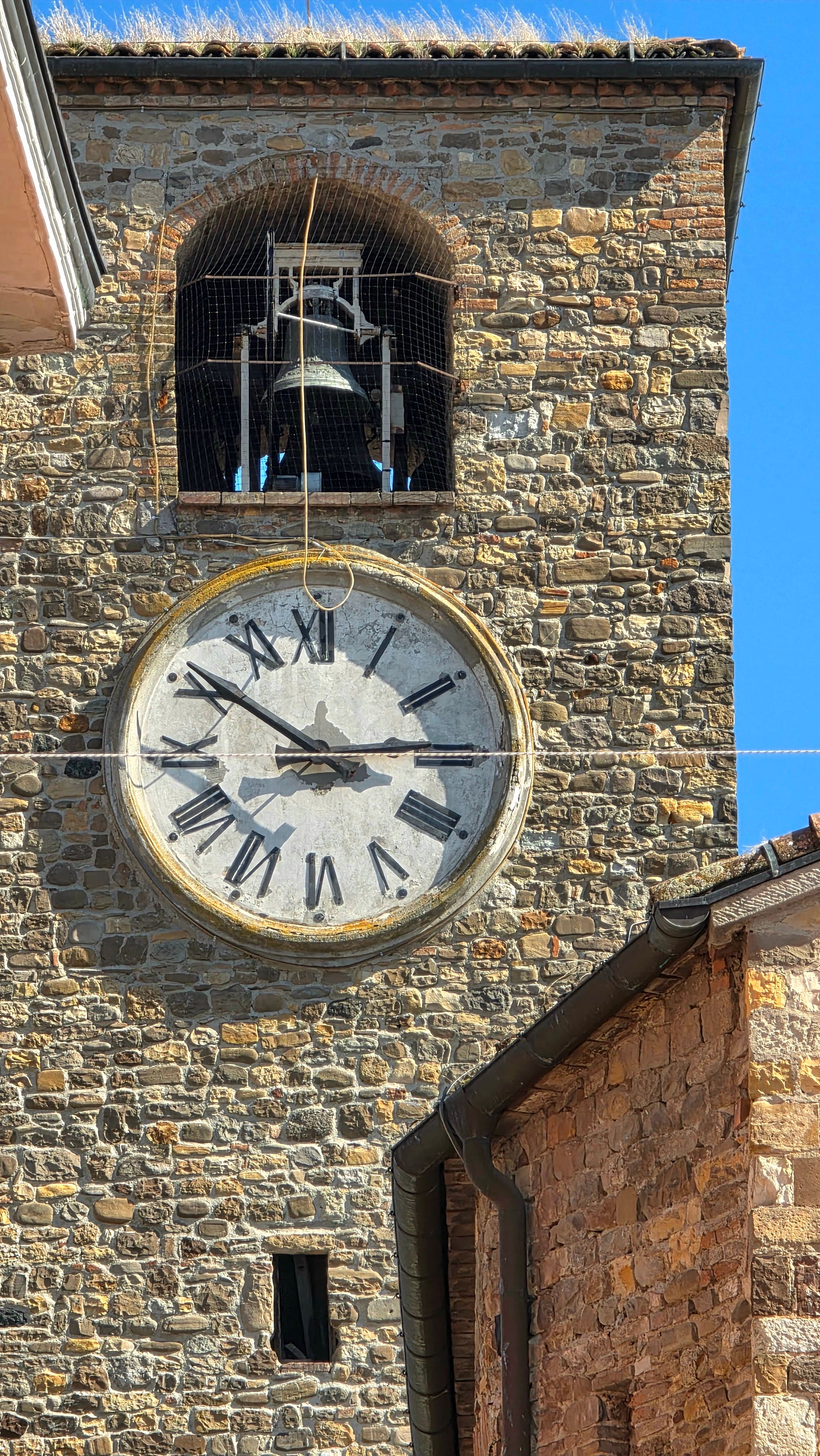 A detailed view of a historic stone clock tower with Roman numerals and visible bell.