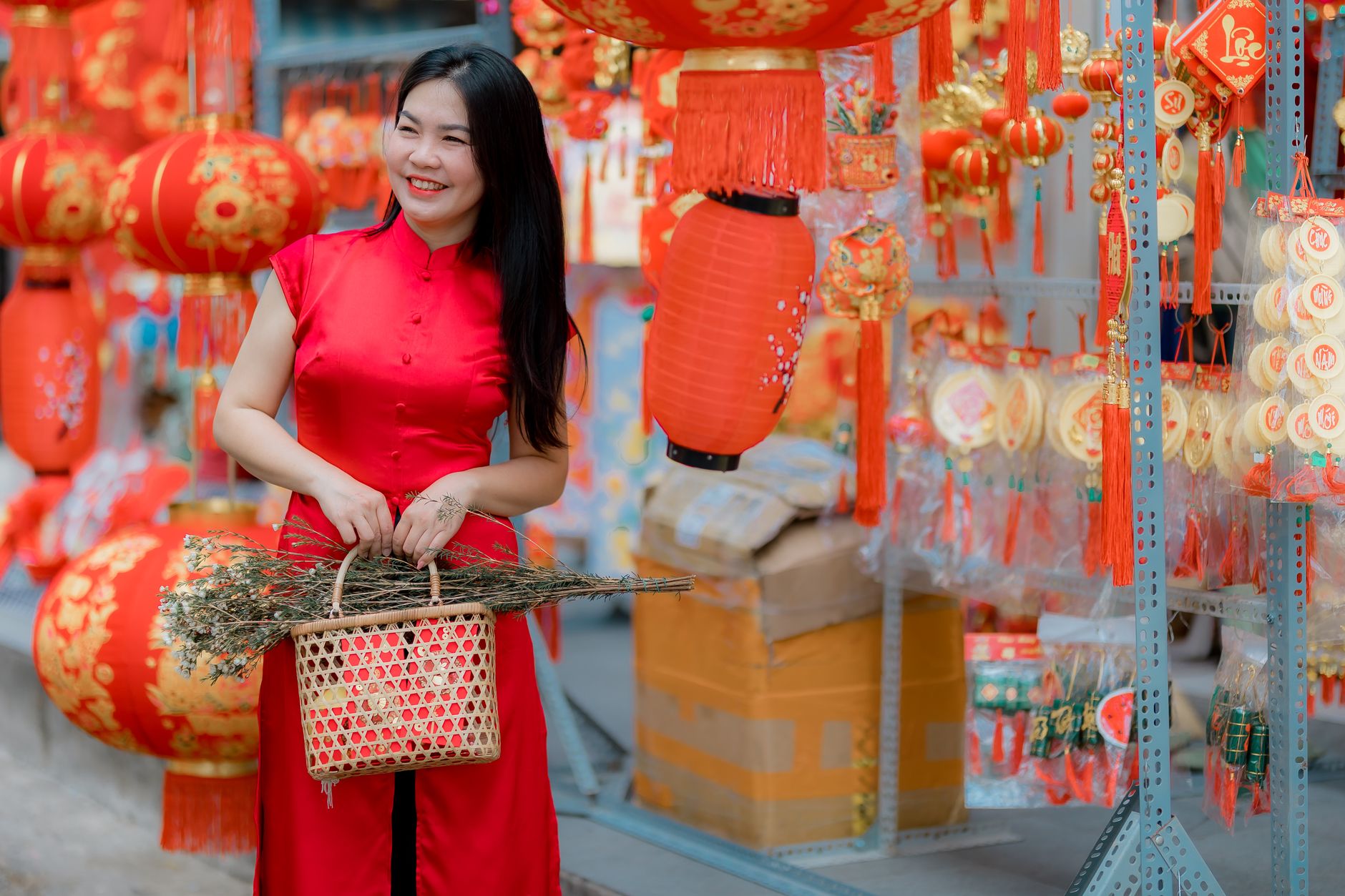 Smiling woman in red dress holds basket among Chinese New Year decorations.