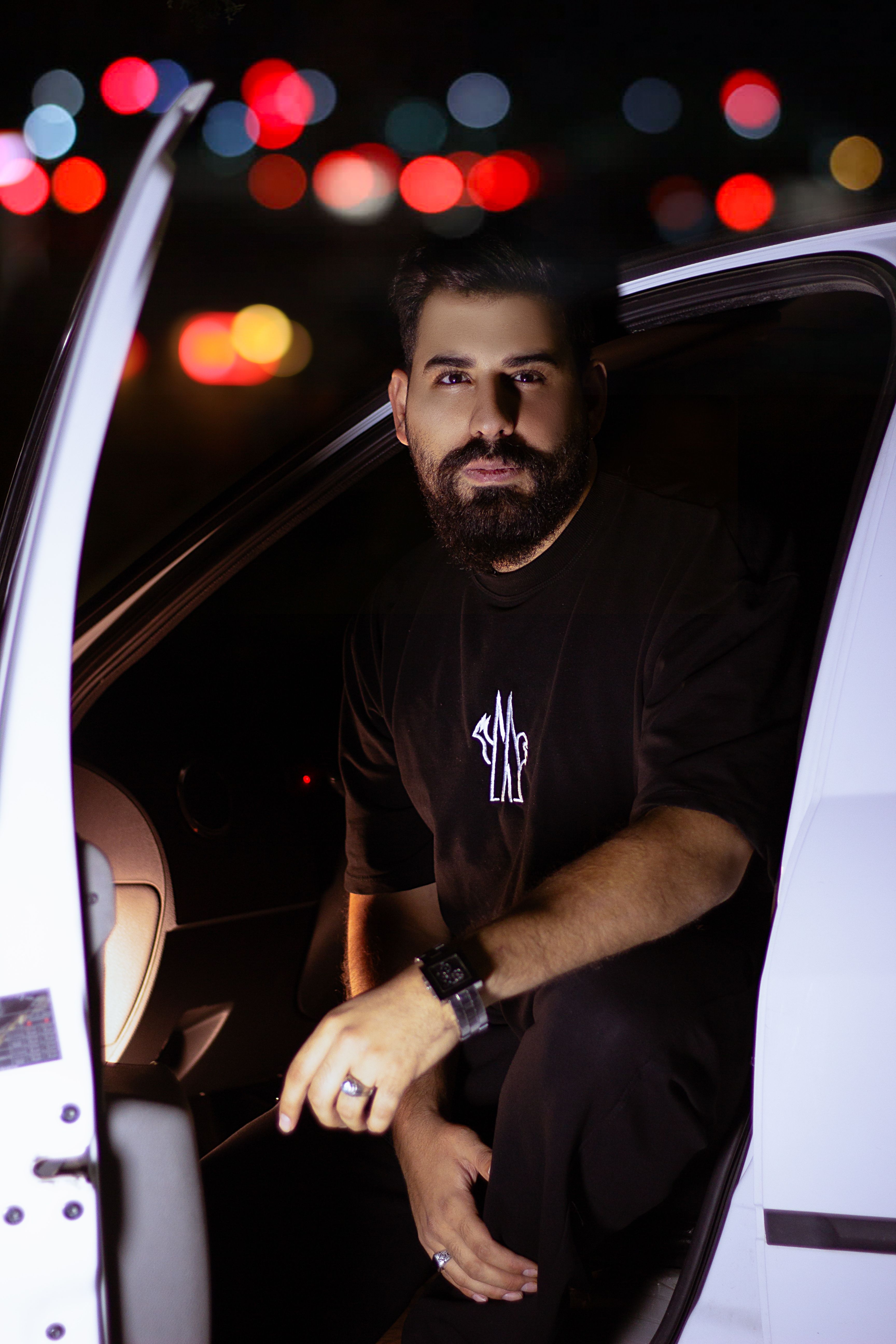 Moody night portrait of a man sitting in a car with city lights in Kermanshah, Iran.