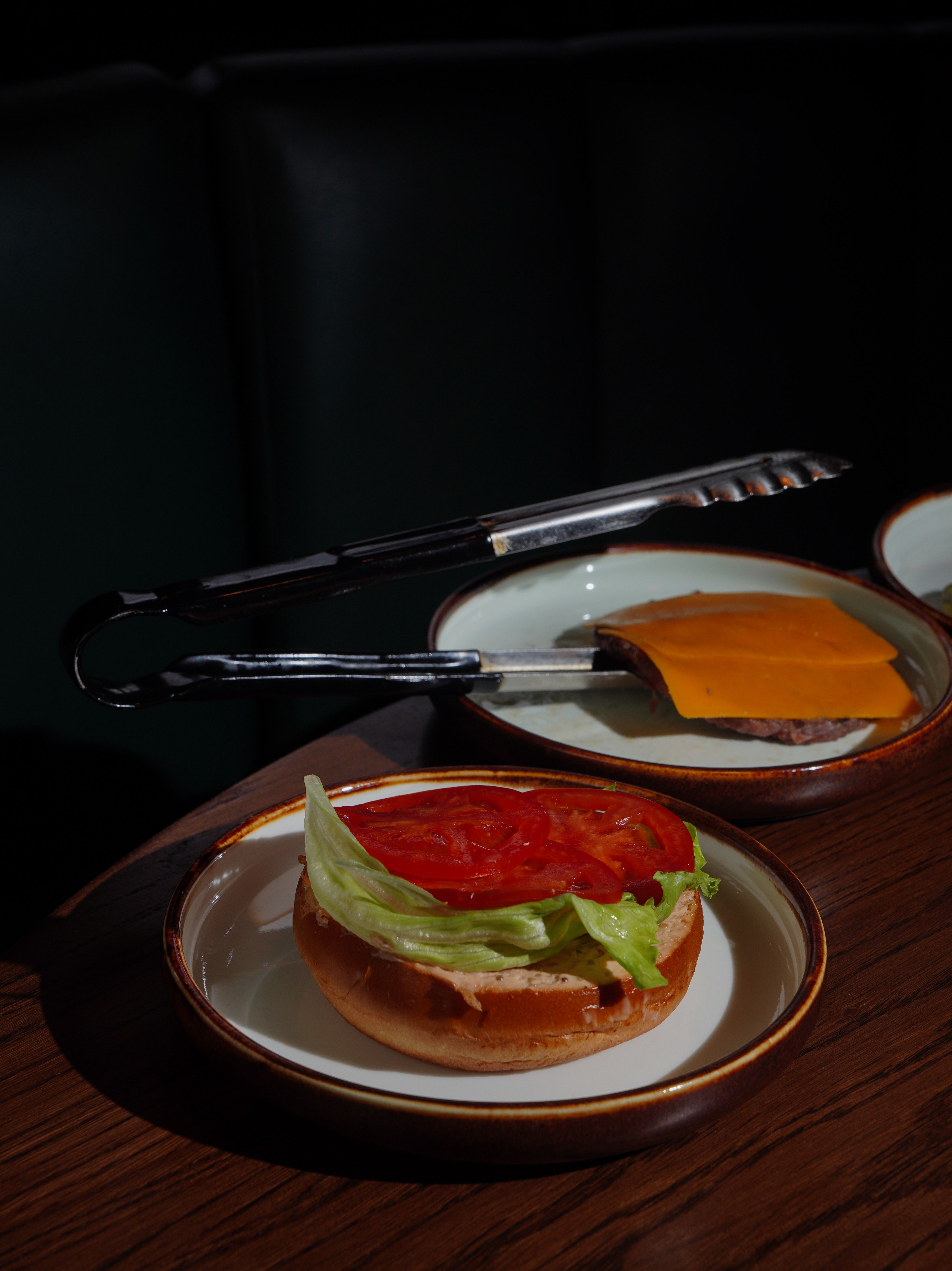 Deconstructed cheeseburger with fresh tomato, lettuce, and cheddar cheese on wooden table.