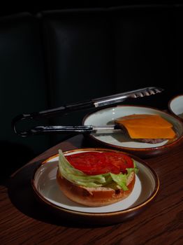 Deconstructed cheeseburger with fresh tomato, lettuce, and cheddar cheese on wooden table.