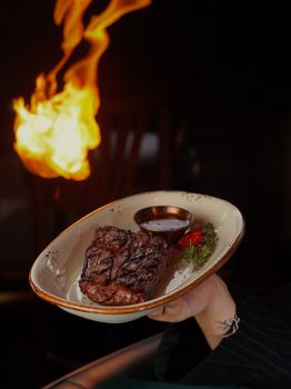 Juicy grilled steak served with sauce and garnish, dramatic flame background enhancing its appeal.
