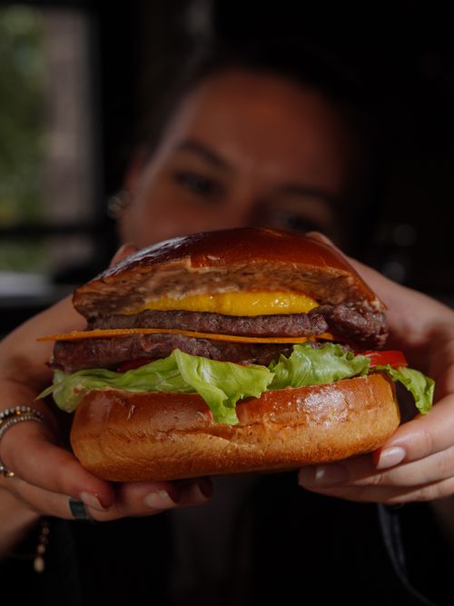 Free Delicious cheeseburger with fresh ingredients held by a person indoors. Perfect for food lovers. Stock Photo