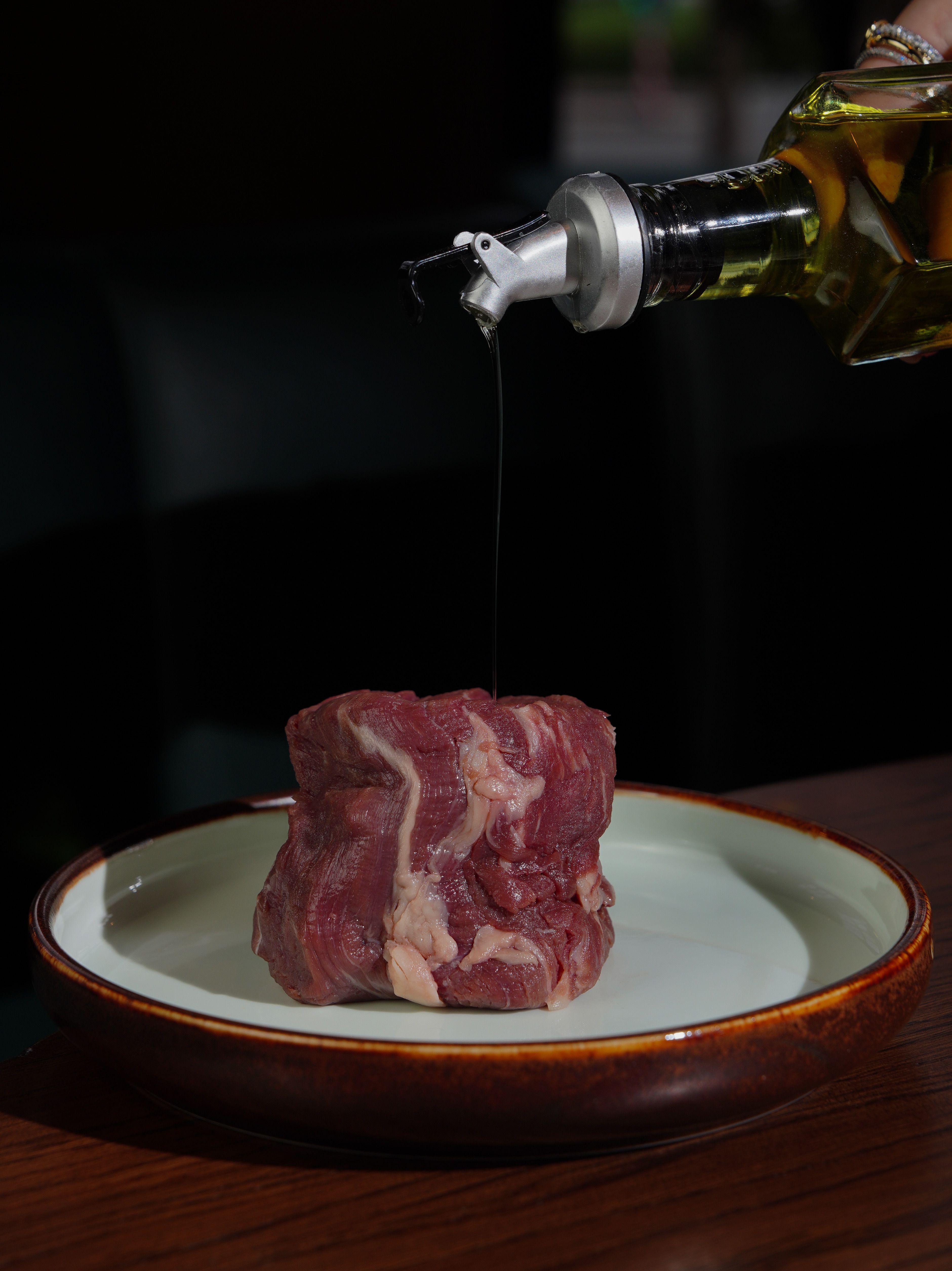 Raw steaks submerged in a dark olive oil and balsamic marinade with garlic cloves and rosemary sprigs in a glass dish.