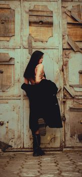 A woman in a dark coat poses against a weathered wooden door, creating a vintage and moody atmosphere.