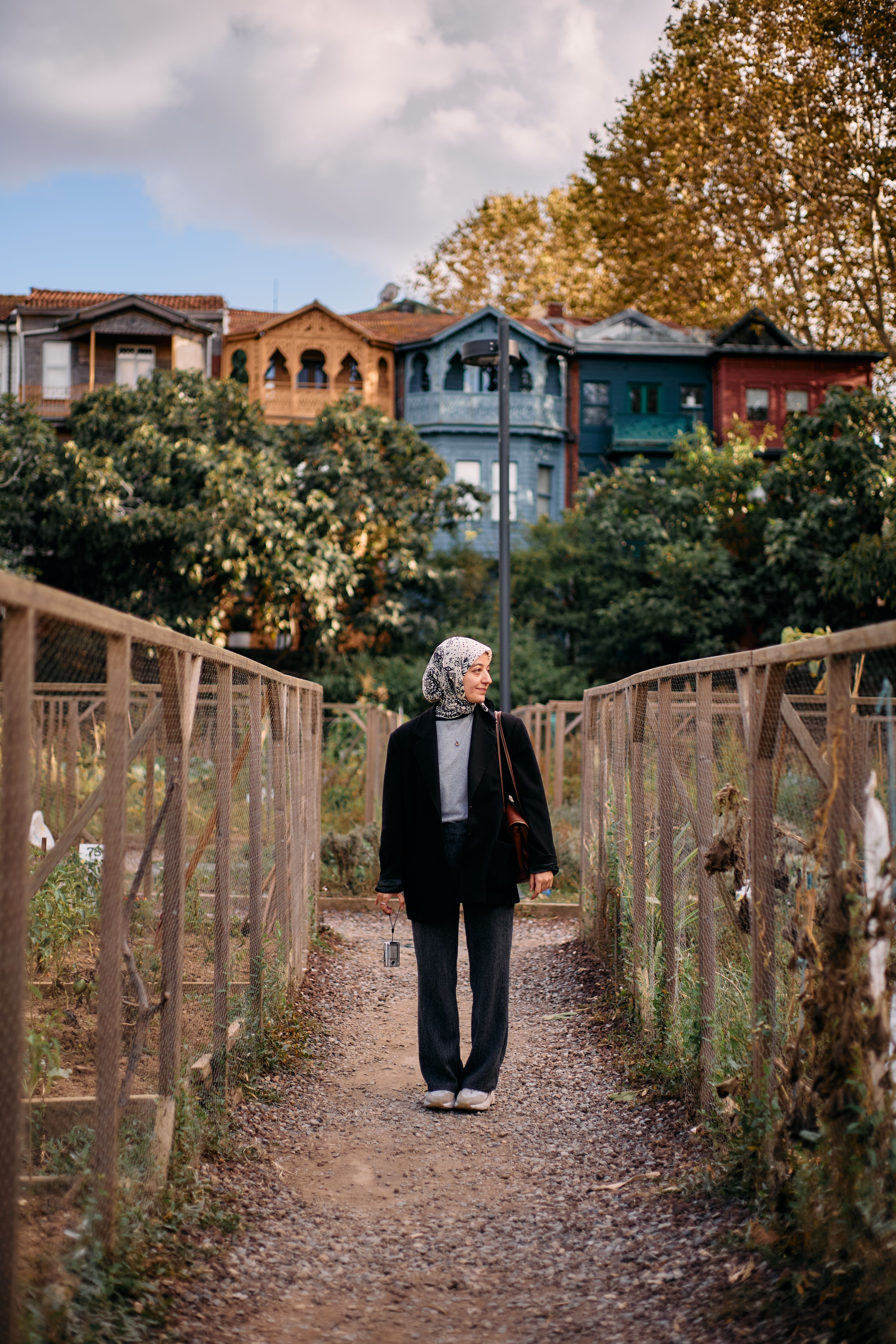 Senior woman explores colorful Istanbul street with traditional houses and autumn foliage.