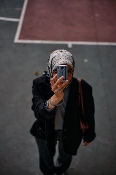 A woman captures a selfie with a vintage camera on an outdoor basketball court in Istanbul.