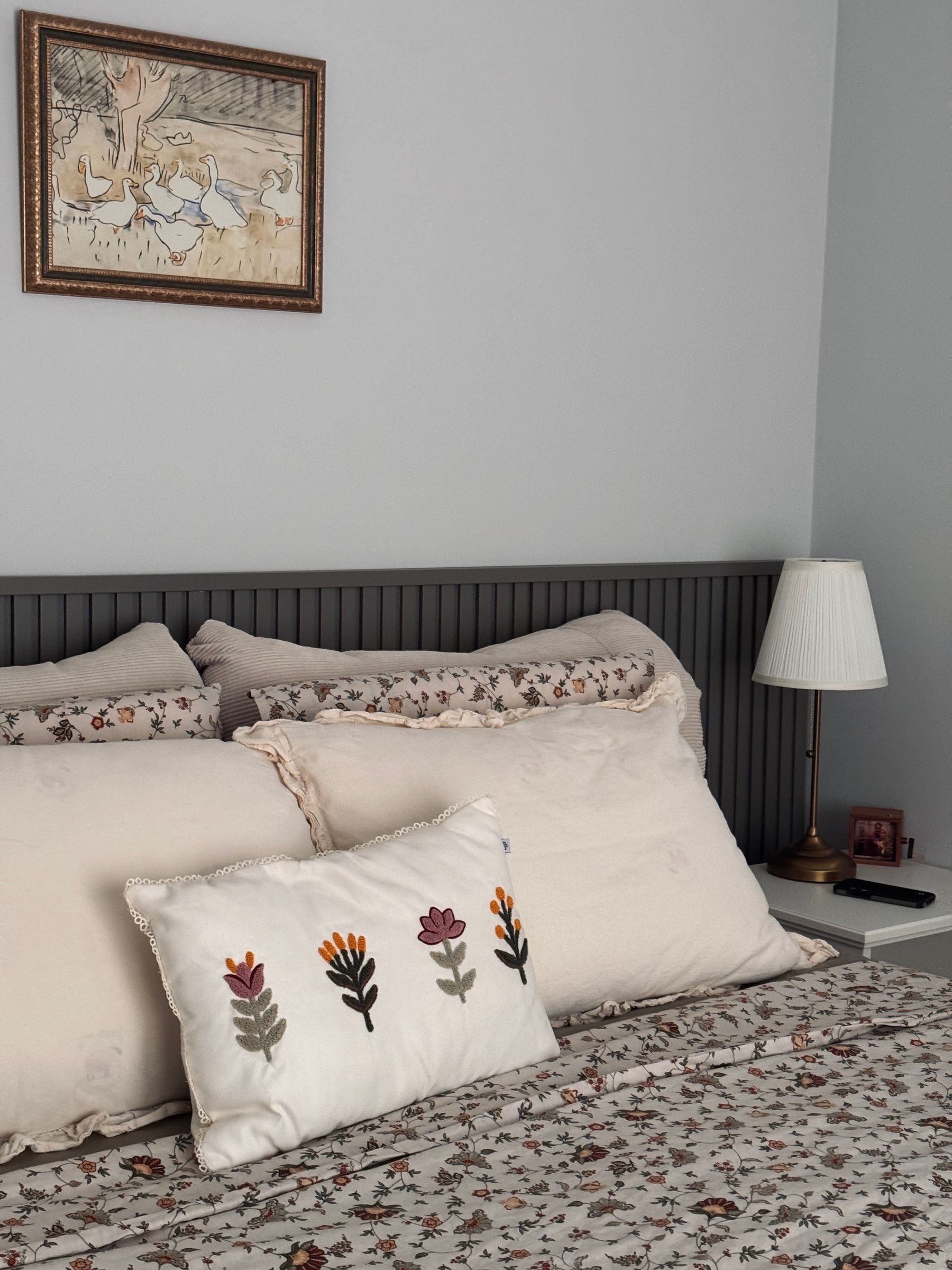 Bed with small floral bedding, white pillows, embroidered botanical cushion and gray slatted headboard