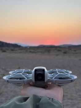 Silhouette of a drone held against a vivid sunset in a desert landscape.