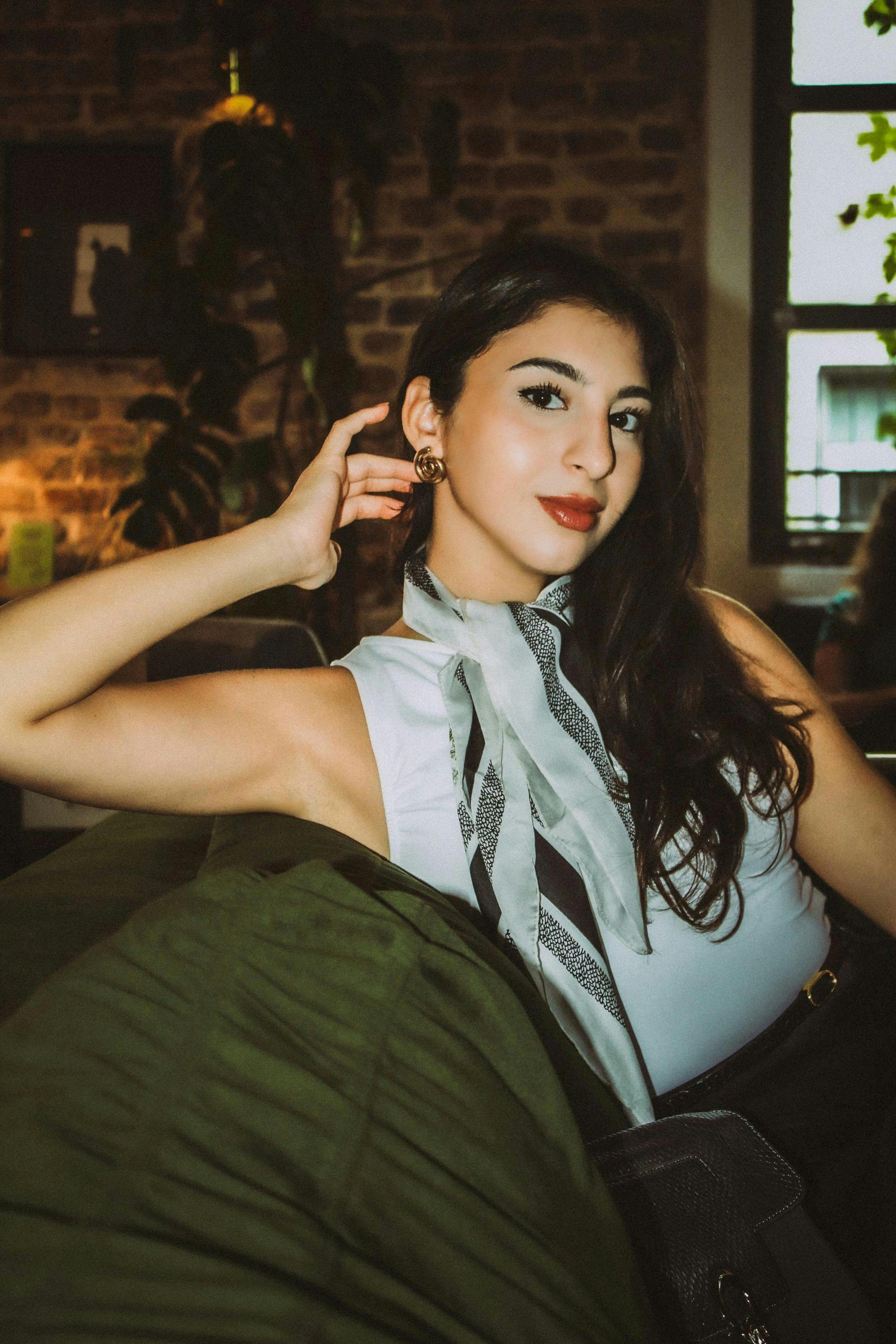 bezplatná Mladá žena v elegantním oblečení, relaxující na pohovce uvnitř, vyzařující eleganci a styl. Základová fotografie