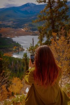A woman photographs autumn foliage in the Colorado mountains, showcasing vibrant fall colors.