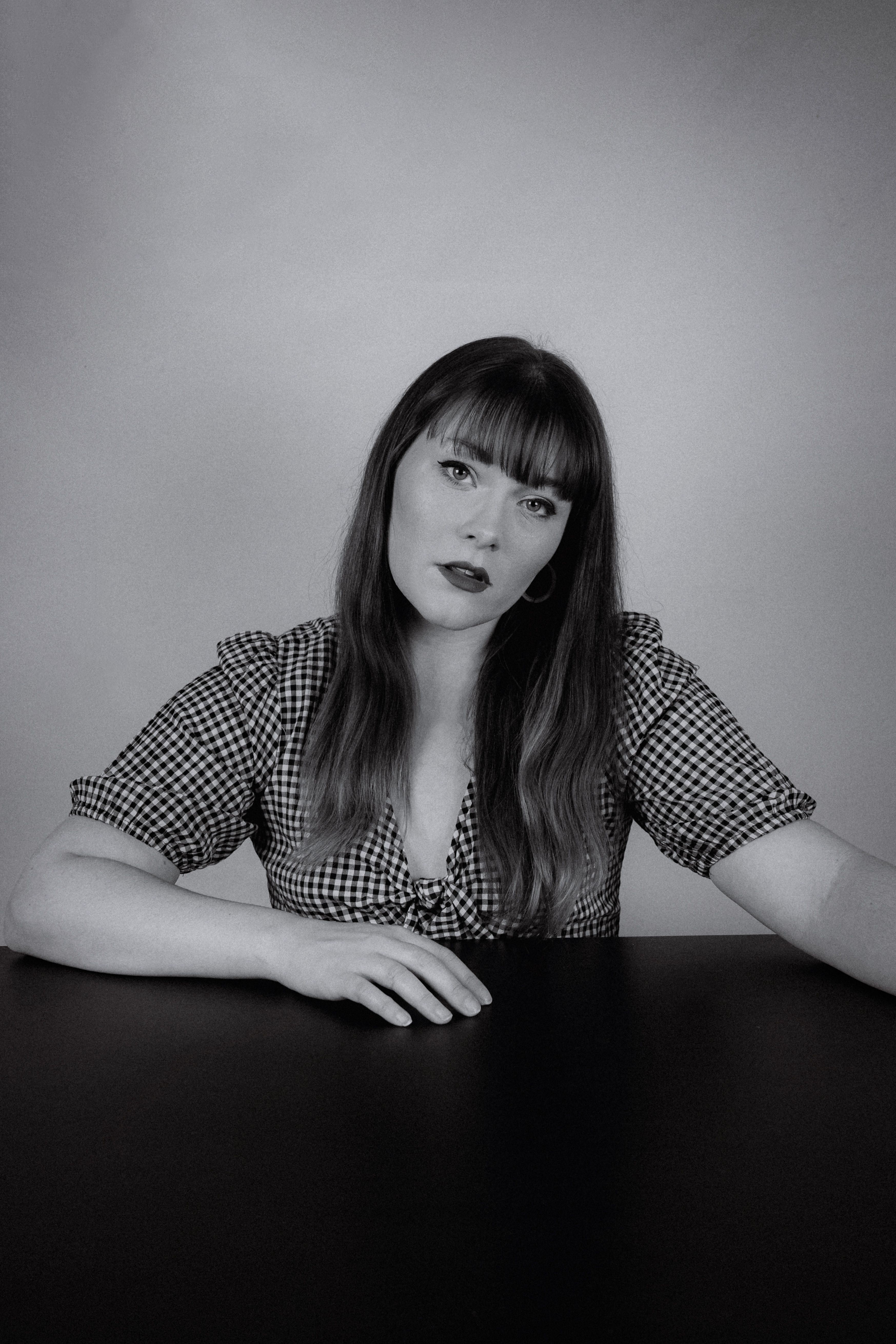 Black and white portrait of a woman with long hair sitting at a table.