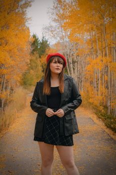 A stylish woman in a black outfit stands amidst vibrant fall foliage in Colorado.