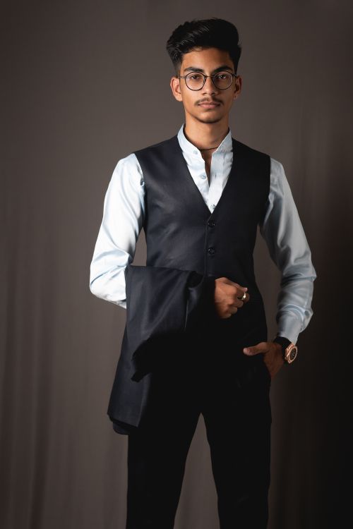 Free Confident young Indian businessman in elegant shirt vest and eyeglasses standing against gray background with hand in pocket and looking at camera Stock Photo
