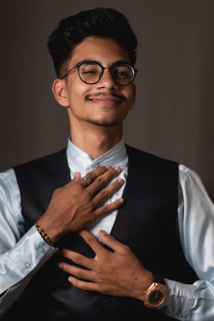 Cheerful Young Indian Guy In Elegant Suit Winking Against Gray Background