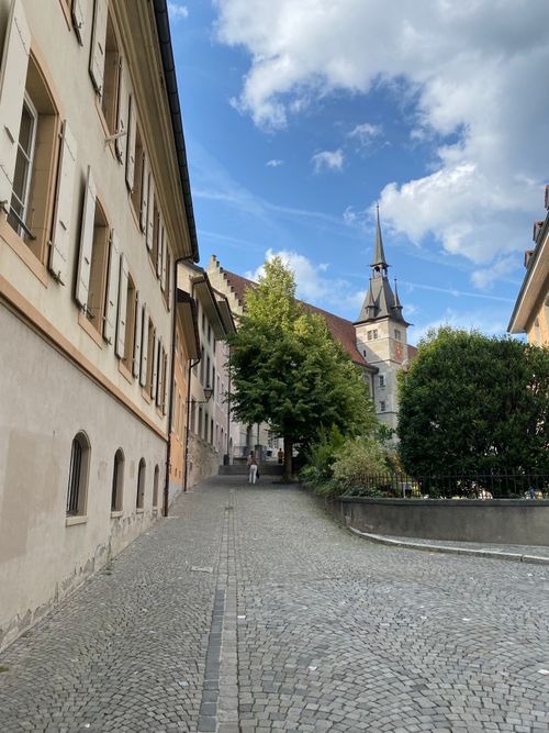Free Discover a quaint European street with historical architecture and a spire-topped church under a blue sky. Stock Photo