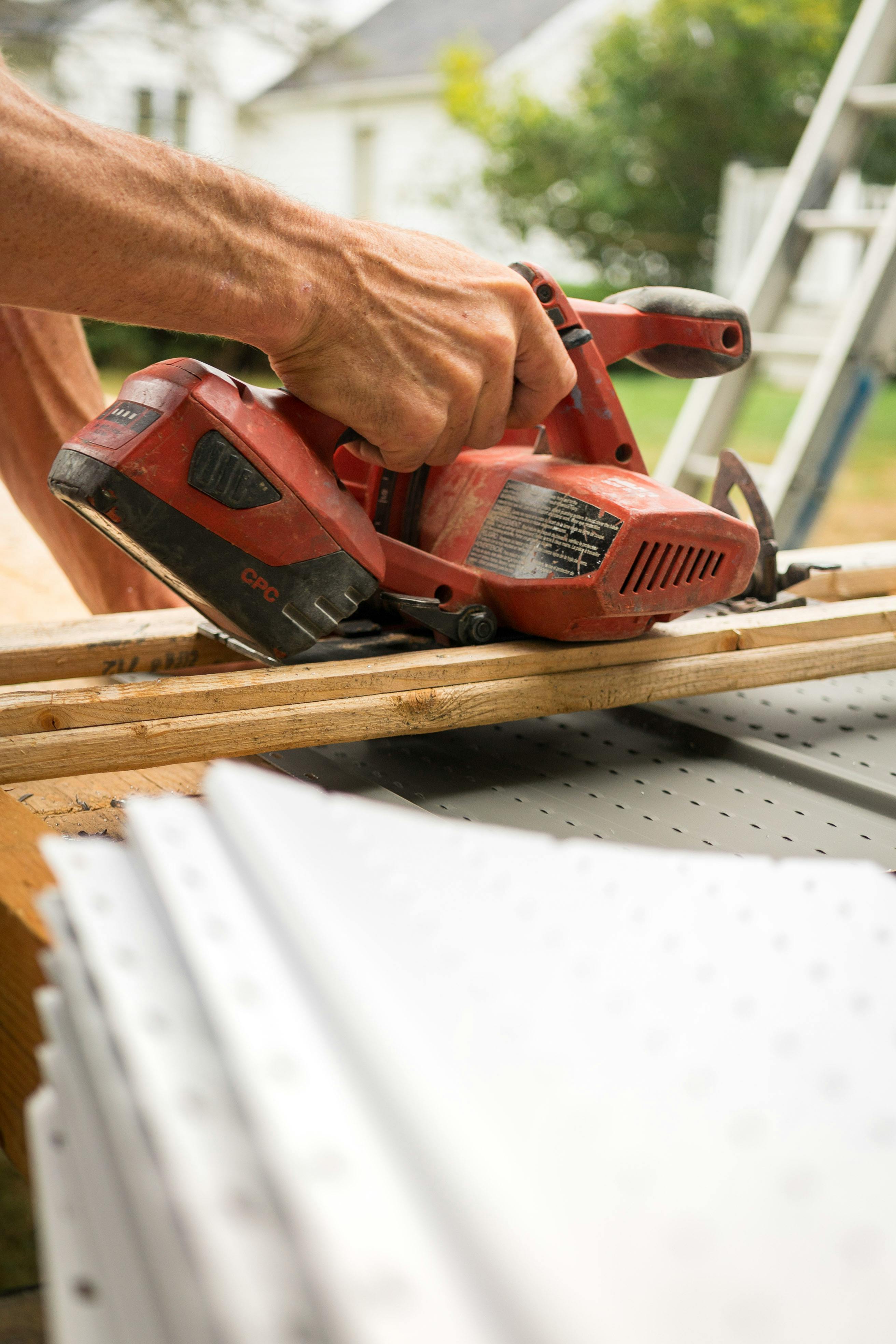 Carpenter using a red electric sander to smooth wood outdoors, showcasing craftsmanship.