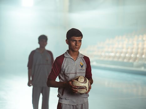 Teenage soccer player holding a ball indoors in Baghdad, showcasing determination and focus.