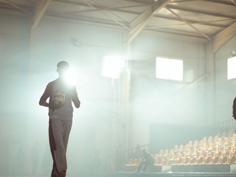 A silhouette of a basketball player holding a ball in a sunlit indoor sports arena.