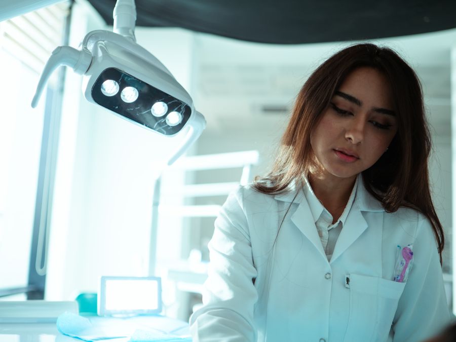 A woman dentist in a white coat under an operating light