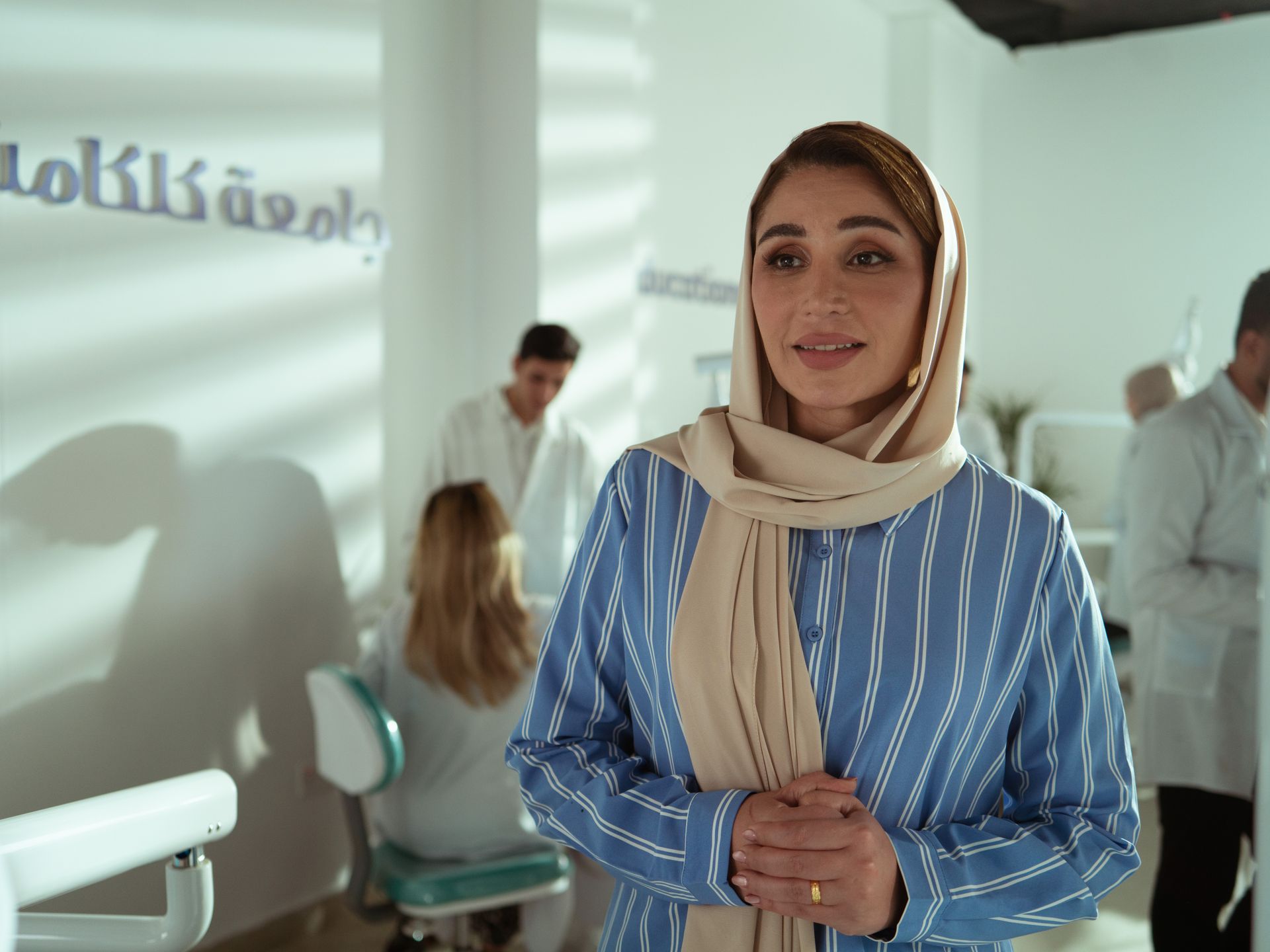 Woman in a striped shirt in an office with colleagues in the background.