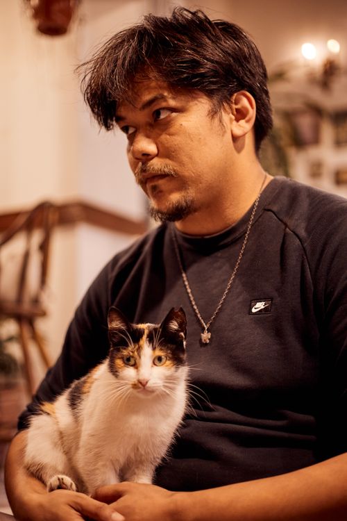 Free A man with a calico cat on his lap, sitting indoors under warm lighting. Stock Photo