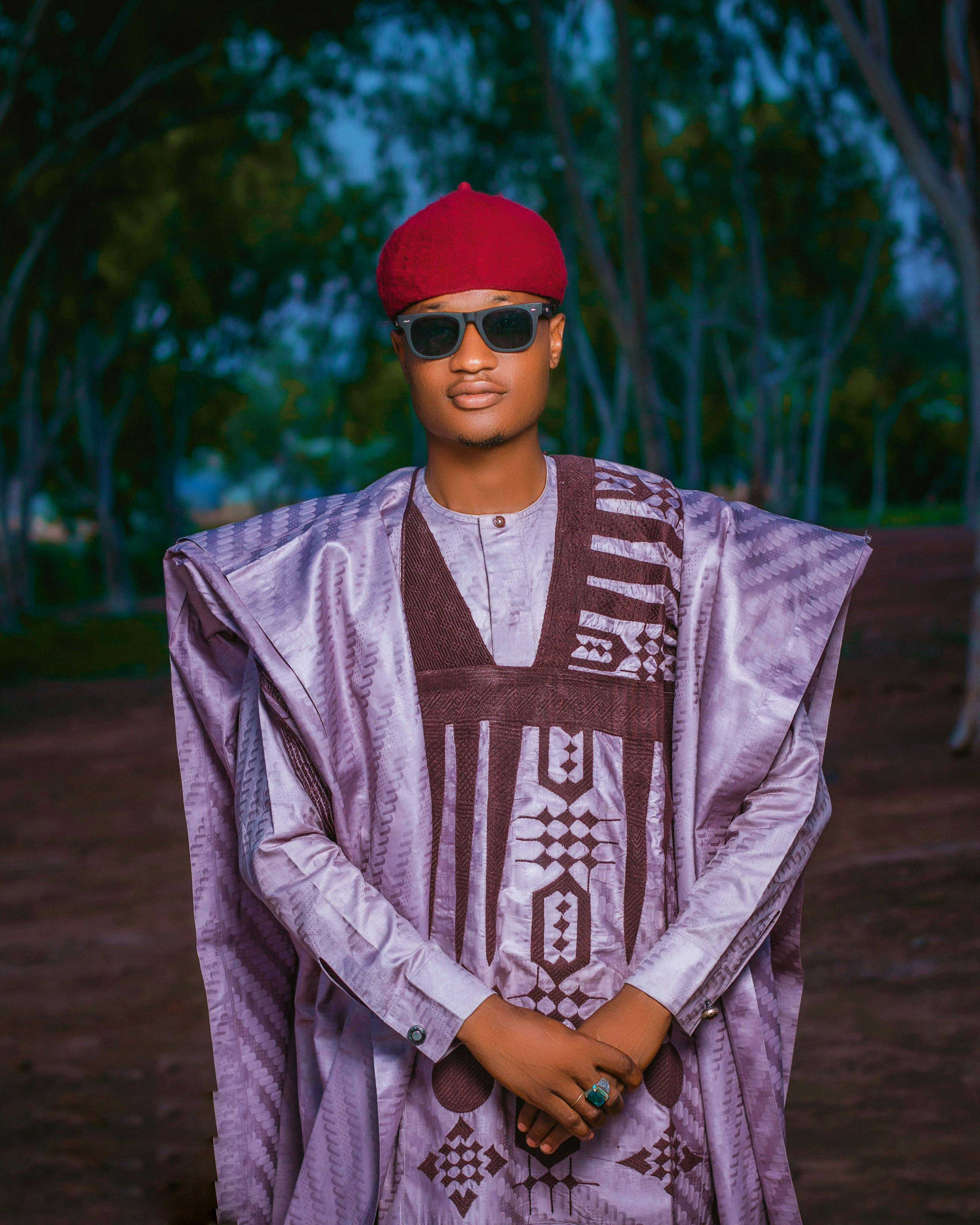 Man wearing traditional Nigerian attire and red cap outdoors, posing confidently.