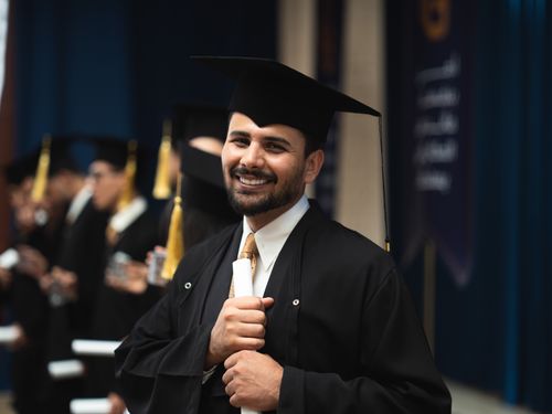 Free A proud male graduate holding his diploma in a cap and gown during a ceremony in Baghdad, Iraq. Stock Photo